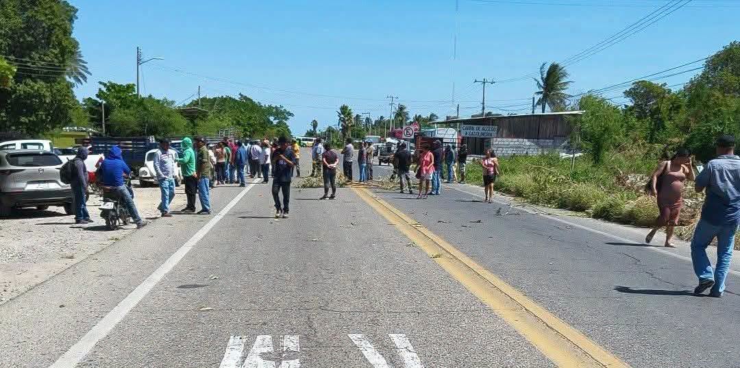 Grupo de personas de pie sobre una carretera con ramas tiradas en el asfalto, bajo un cielo despejado