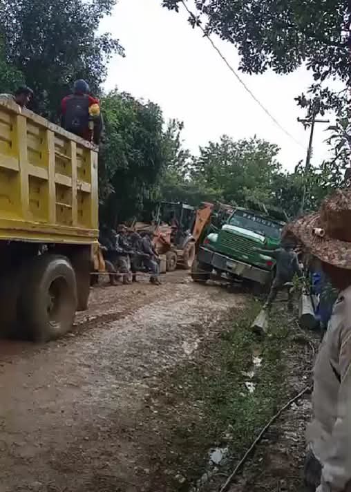Volteo amarillo con personas, retroexcavadora y camión verde en un camino de terracería enlodado